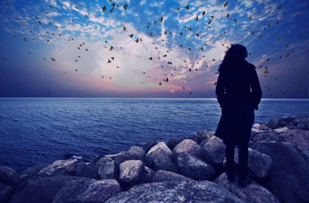 امراة تقف على الصخر وحيدة امام البحر